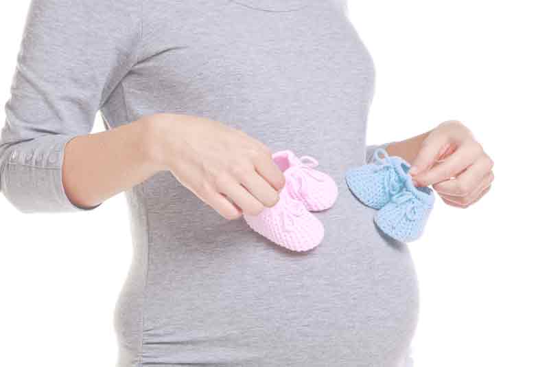 Eine schwangere Frau mit Babyschuhen in der Hand in den Farben Rose und Blau